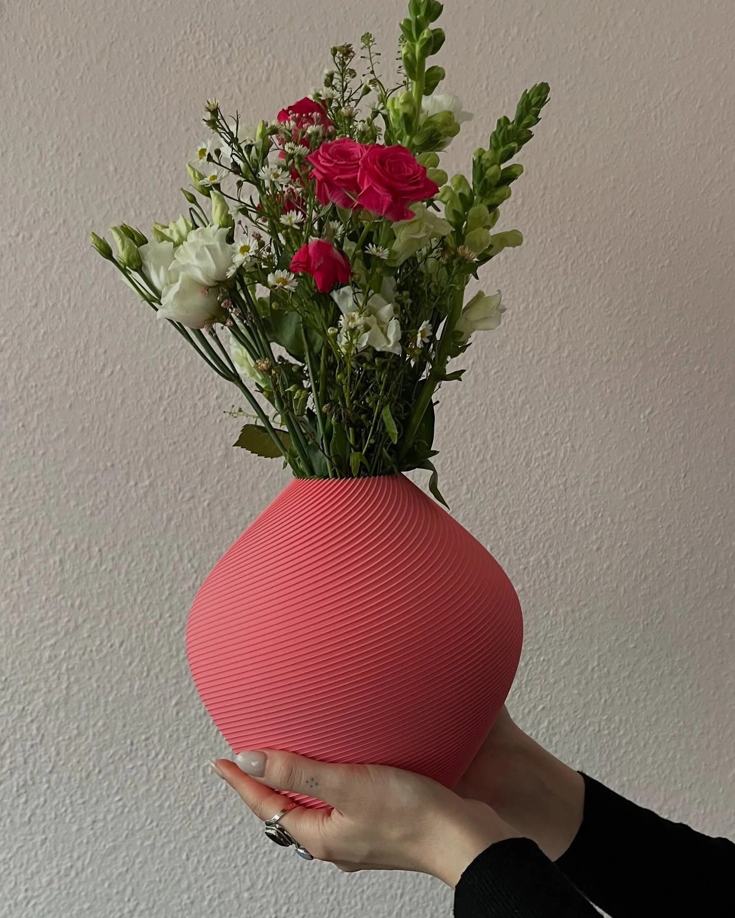 Hand holding a coral vase filled with spring flowers
